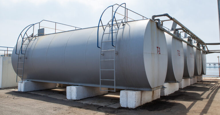 Four horizontal cylindrical tanks sit next to each other, surrounded by other equipment, structures, and a fence.