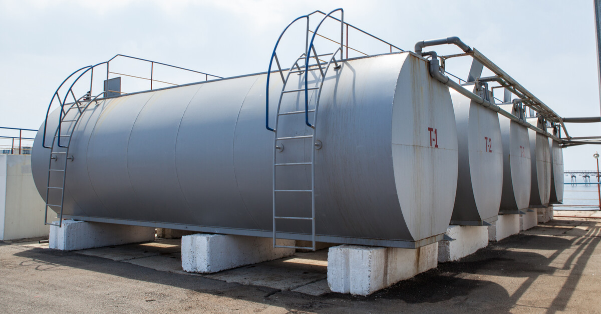 Four horizontal cylindrical tanks sit next to each other, surrounded by other equipment, structures, and a fence.