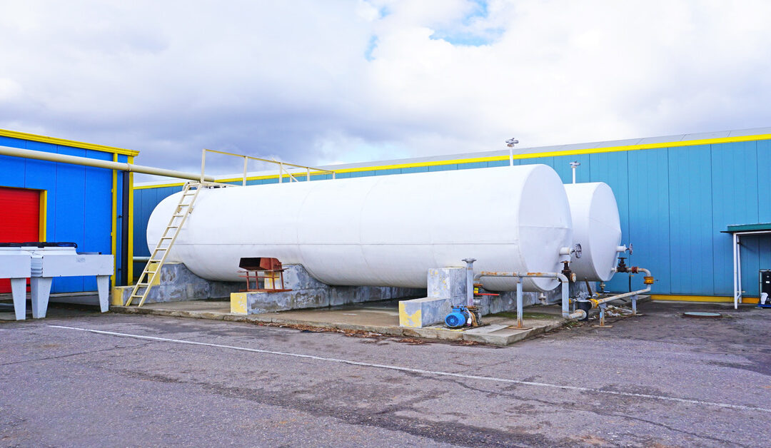 A close-up of a two large storage tanks outside of a building. The building is blue and the tanks are white.