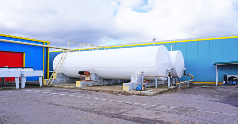 A close-up of a two large storage tanks outside of a building. The building is blue and the tanks are white.