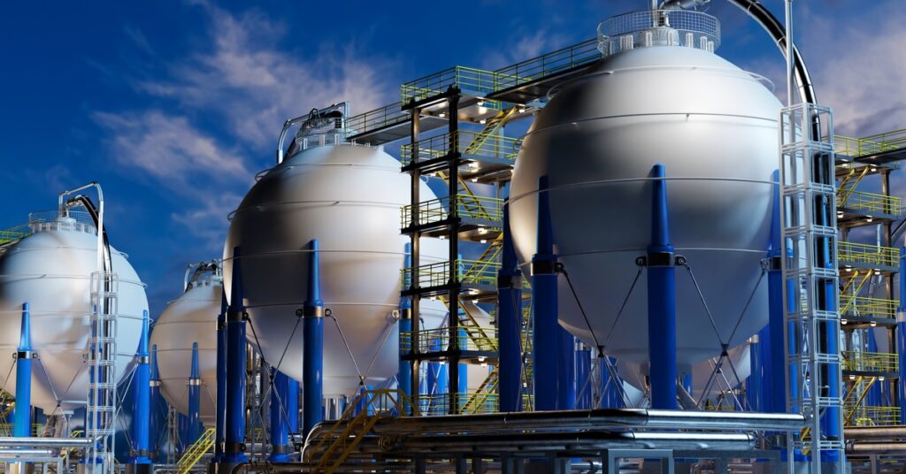 Silver and blue spherical storage containers are surrounded by scaffolding and staircases. Grass covers the ground.