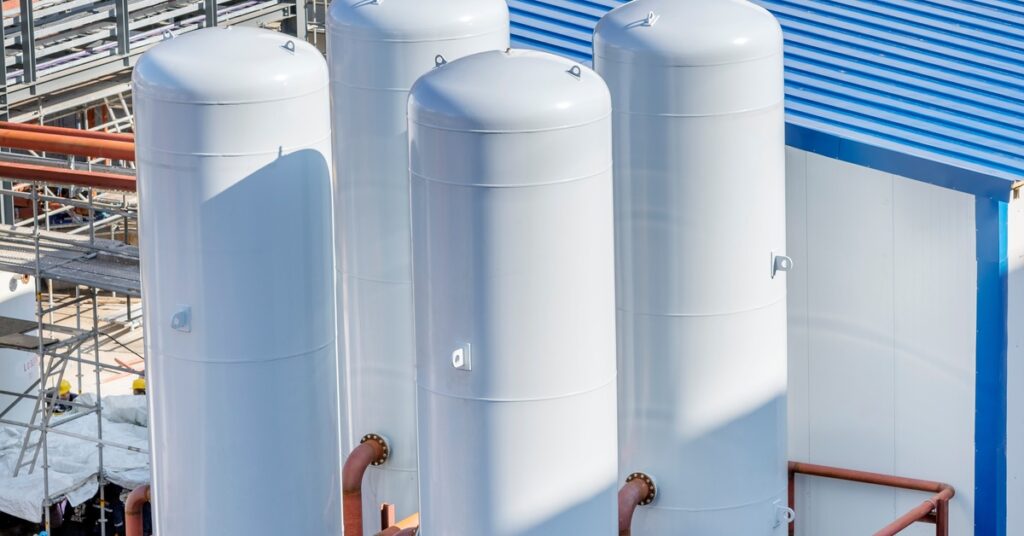 Four tall vertical cylindrical storage tanks standing next to each other on top of concrete in a construction site.