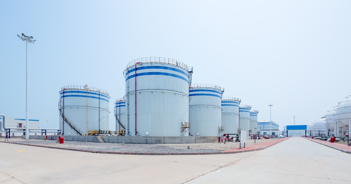An oil depot with numerous rows of large cylindrical storage tanks with blue stripes near the top.