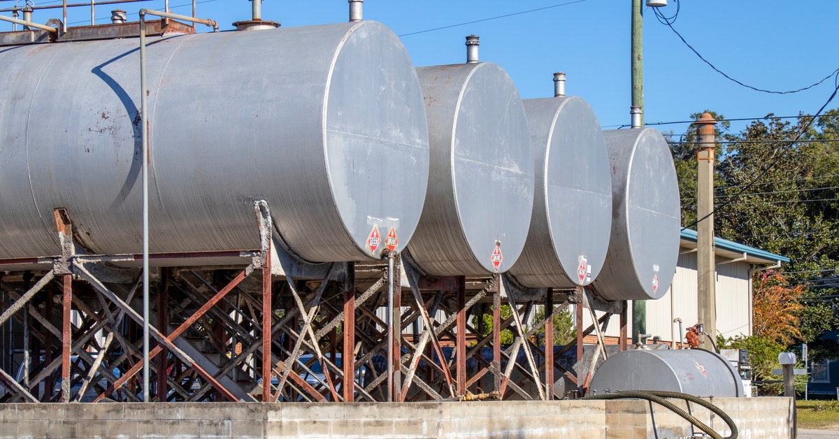 Four large storage tanks sitting next to each other on top of some steel supports. There are power lines and a telephone pole in the background.