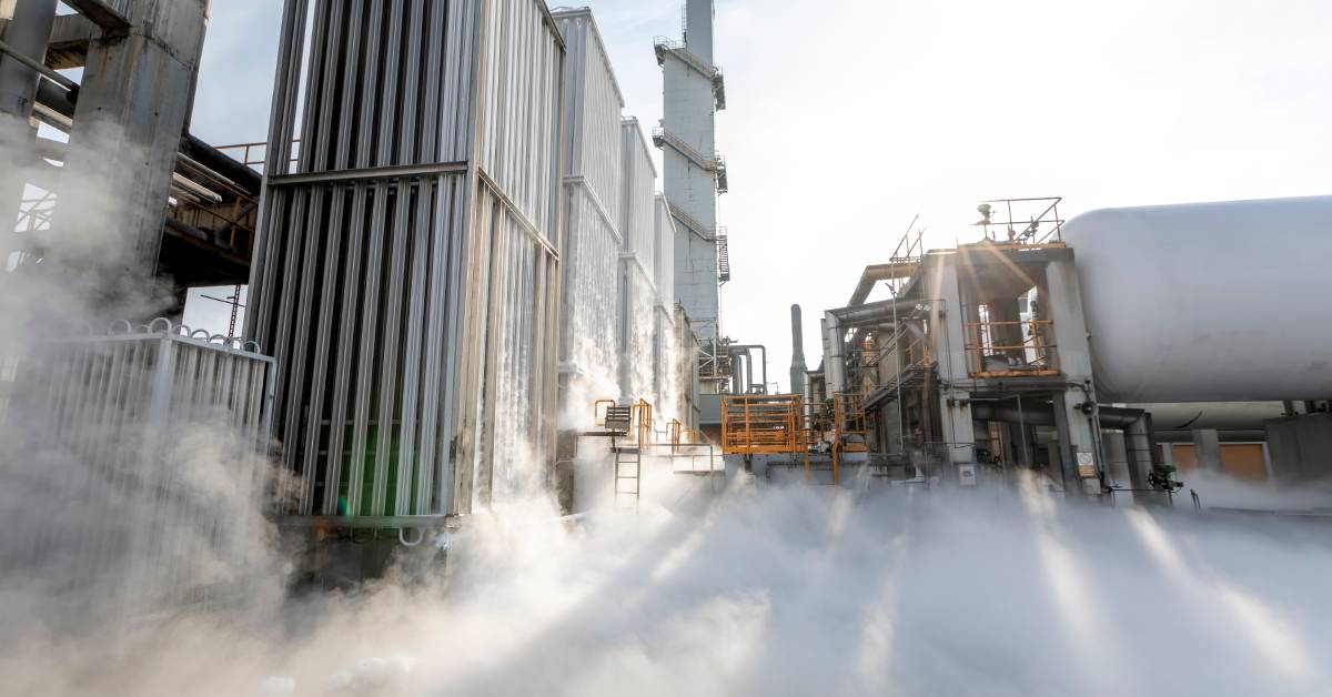 An outdoor work area with some large storage tanks next to other industrial equipment. Mist if forming on the ground between the tanks.