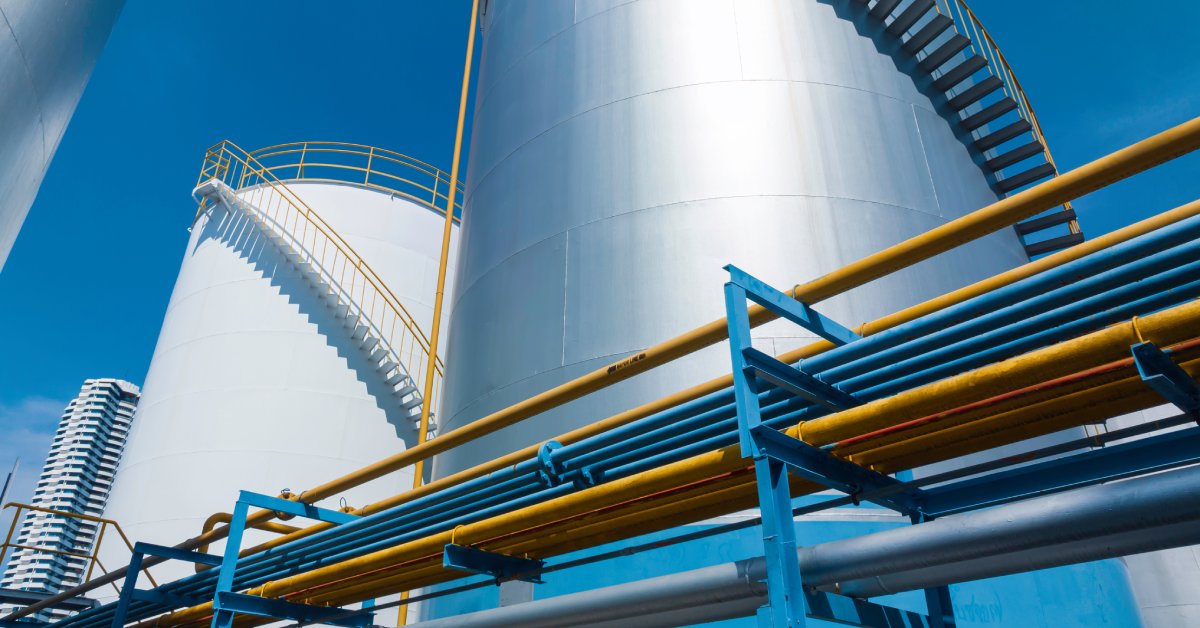 Two tall storage tanks stand next to each other with staircases going up the sides. These tanks are next to some pipes.