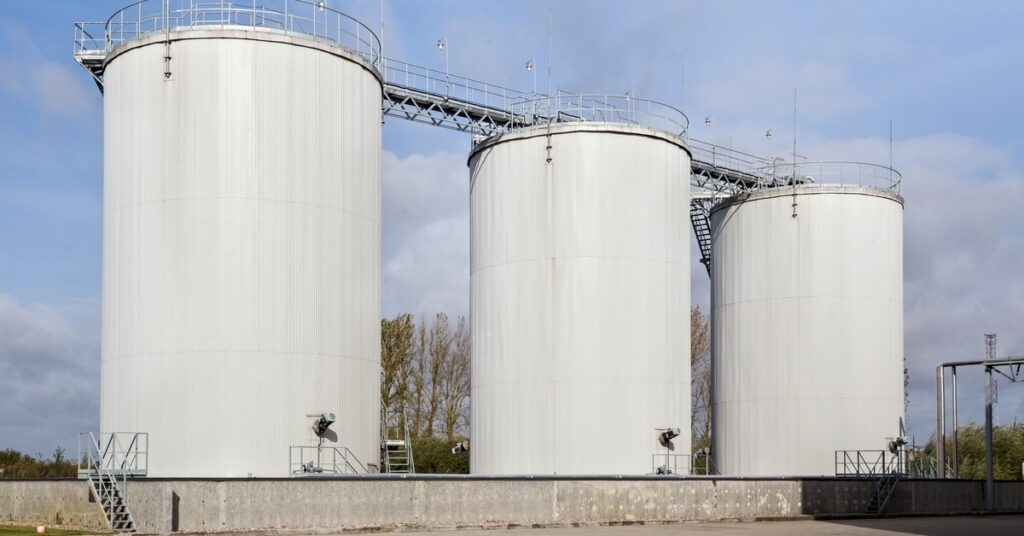 Three large white storage tanks stand next to each other with winding staircases running up to the top of each.
