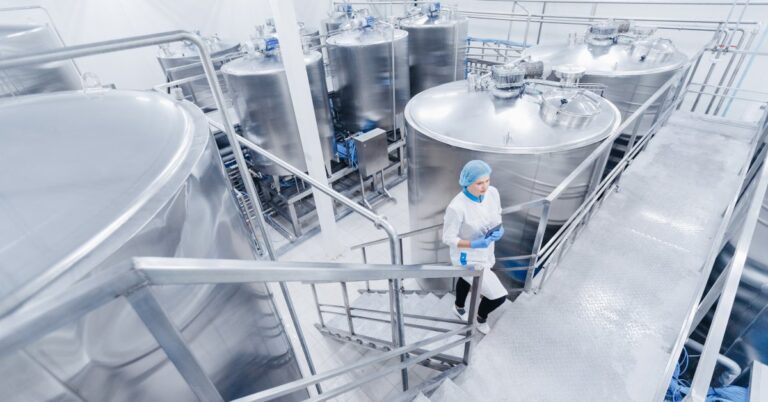 A food processing facility where material tanks are gathered. A woman wearing a coat and hair net walks up the stairs.