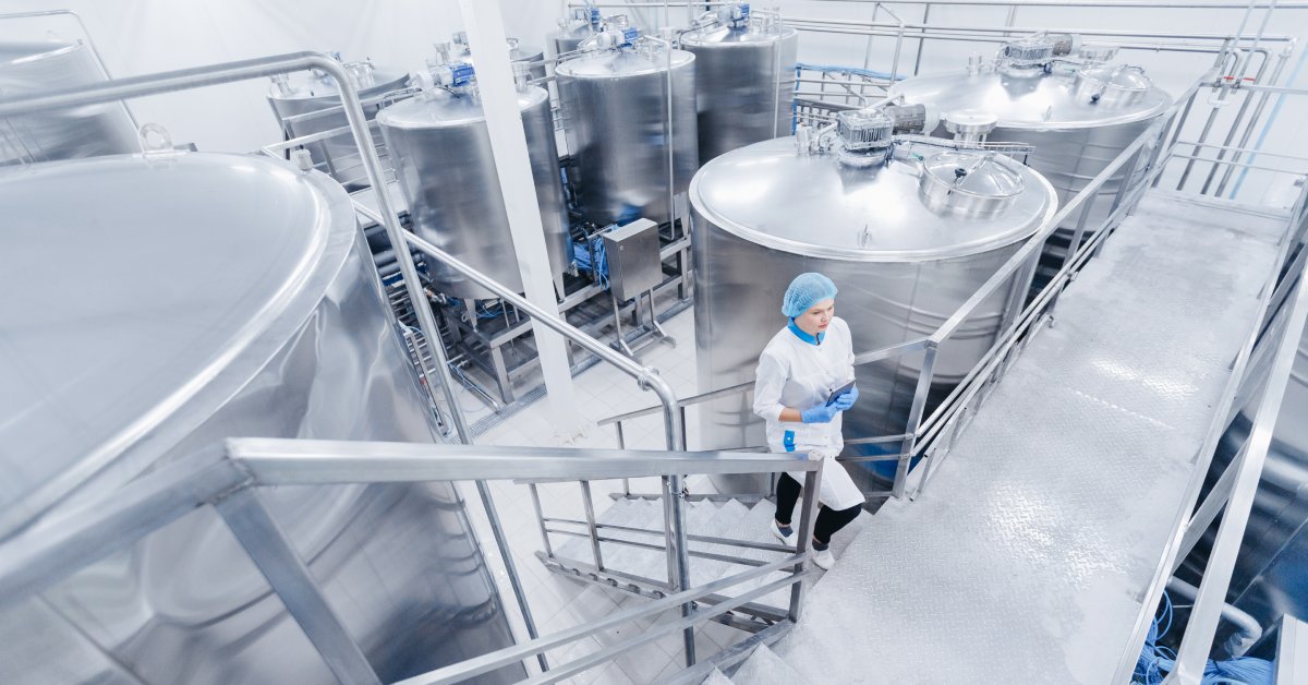 A food processing facility where material tanks are gathered. A woman wearing a coat and hair net walks up the stairs.