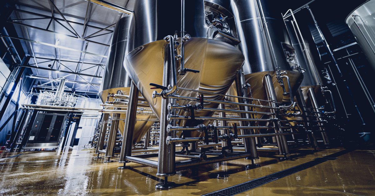 A ground-up view of large, steel tanks in a processing plant with various matching pipes connecting them.