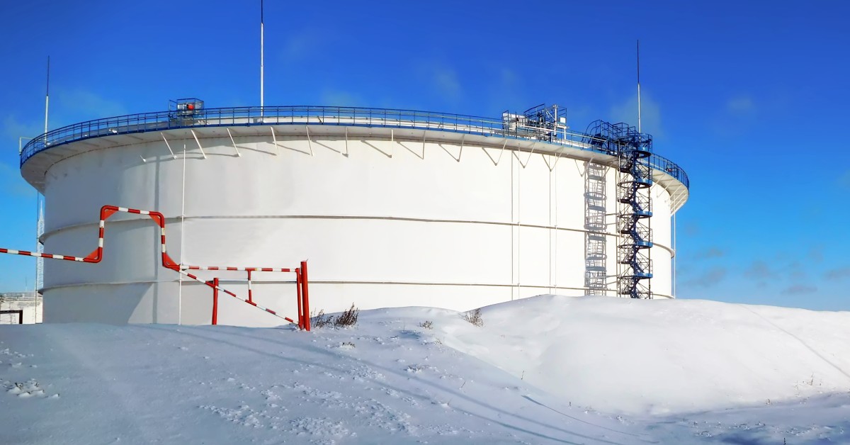 A large white, industrial containment tank on a snowy landscape with a blue sky in the background.