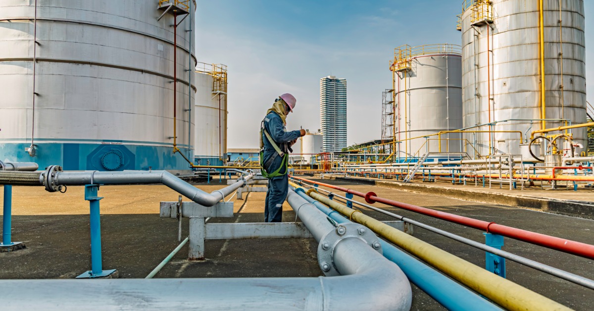 A person wearing protective gear and a hard hat at a facility with several water tanks set around pipes.
