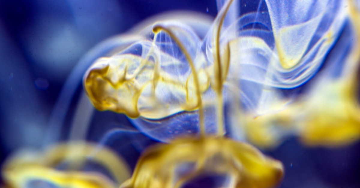 A chemical mixing with water, a yellow streak of liquid mixing with the clear water background.