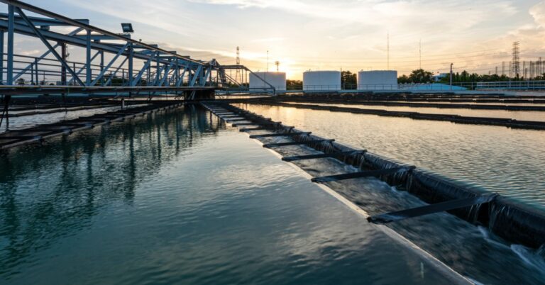 a wide view of circular water treatment tanks with walkways, dark liquid, and industrial equipment outdoors.
